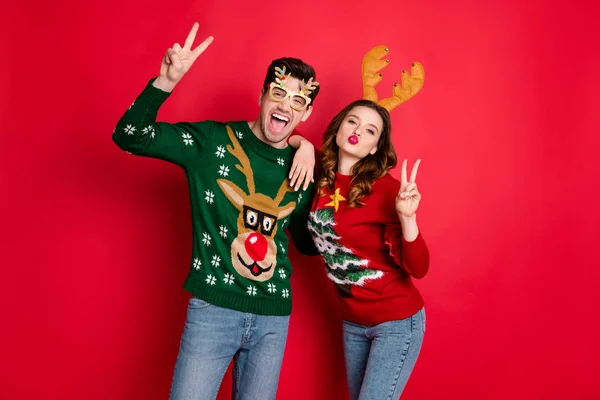 Портрет сумасшедших двух семейных людей жена мужа каштановые волосы худые плечи сделать V-знаки отправить воздушный поцелуй губы надутые носить смешные рога рождественские очки одежды, изолированные на красный цвет фона — стоковое фото