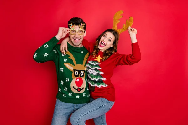 Portrait of crazy two people wife husband student hipster hug embrace wear brown comfort cozy pullover sweater with chritsmas tree design denim jeans eyewear isolated over red color background — Stock Photo, Image