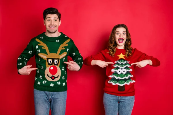 Midnight presents. Portrait of two brunet hair lovers people scream wow omg point indexf inger his her reindeer christmas tree pattern pullovers wear jeans isolated over red color background — Stock Photo, Image