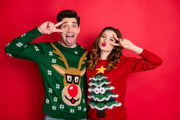 Portrait of two funky people hipsters make v-signs grimace send air kisses wear seasonal reindeer christmas tree design sweater jumper isolated over red color background — Stock Photo, Image