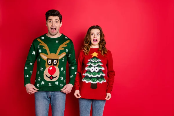 Portrait of frustrated frightened two youth people with brunette wavy hair dislike christmas tree pattern decor jumper shout omg wear denim jeans isolated over red color background — Stockfoto