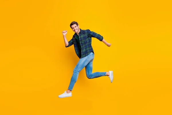 Úplná délka těla fotografie veselého přitažlivého chlápka, který skáče někam, kde módní nosí džíny, izolované přes živé barevné pozadí — Stock fotografie