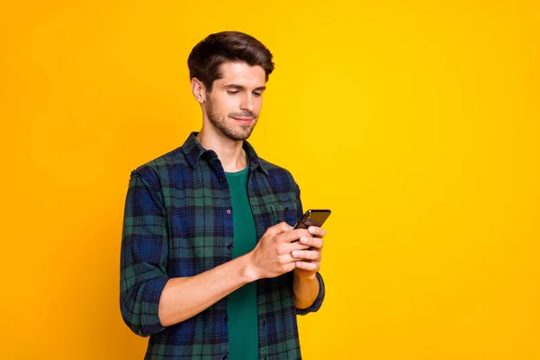 Photo of blogger guy holding telephone in hands checking subscribers wear casual checkered shirt isolated yellow color background