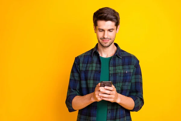 Photo of blogger guy holding telephone in hands checking instagram followers wear casual checkered shirt isolated yellow color background