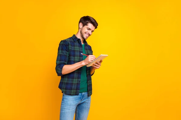 Foto de perfil de buen tipo con organizador en las manos haciendo notas creando idea de inicio usar camisa a cuadros casual y pantalones vaqueros aislados de color amarillo fondo — Foto de Stock