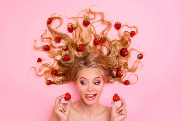 Nahaufnahme oben über Hochwinkel-Ansicht Foto schön sie ihre Dame liegend zwischen Obst Erdbeeren lange Haare pflücken zwei Beeren wollen essen eifrige Zunge aus dem Mund isoliert rosa Hintergrund — Stockfoto