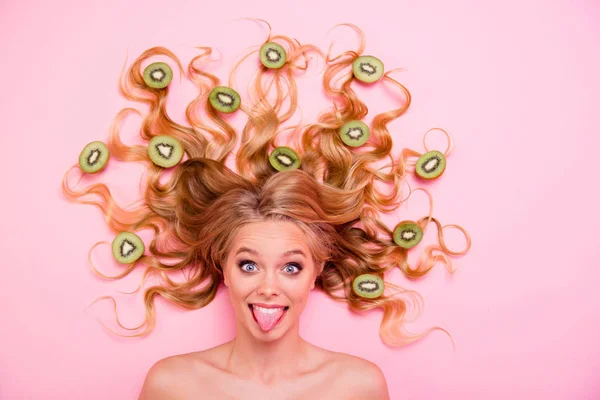Close up top above high angle view photo beautiful she her lady lying down full kiwi fruits pretty long curls healthy lifestyle tongue out mouth playful mood salon procedure isolated pink background — Stock Photo, Image