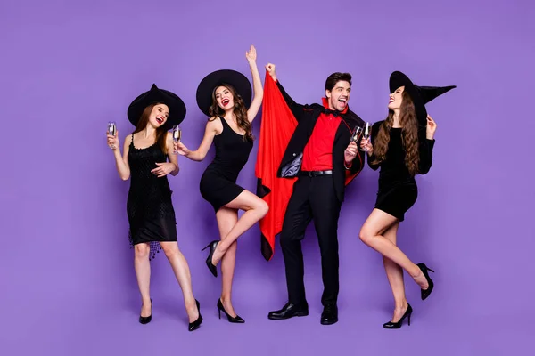 3 명의 마녀 숙녀와 마법사 남자가 황금 와인을 마시는 춤을 추는 클럽의 전신 사진 은 검은 드레스 모자 정장과 긴 코트 고립 된 보라색 색상 배경 — 스톡 사진