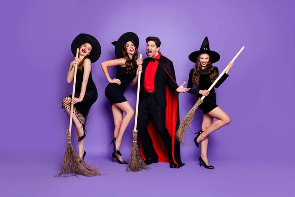 3人の魔女の女性と魔法使いの男ロックバンドのフルボディ写真は、黒いドレスキャップスーツと長いコート孤立した紫色の背景を着用して歌を歌うほうきを保持します — ストック写真