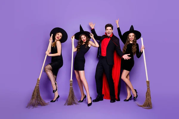 テーマの学生パーティーを配置するほうきを持つ3人の魔女の女性とウォーロックの男のフルボディ写真は、短いドレスの帽子と長いコート孤立した紫色の背景を着用 — ストック写真
