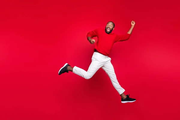 Foto de cuerpo entero del chico alegre saltando levantando las manos gritando usando jersey aislado sobre fondo rojo — Foto de Stock