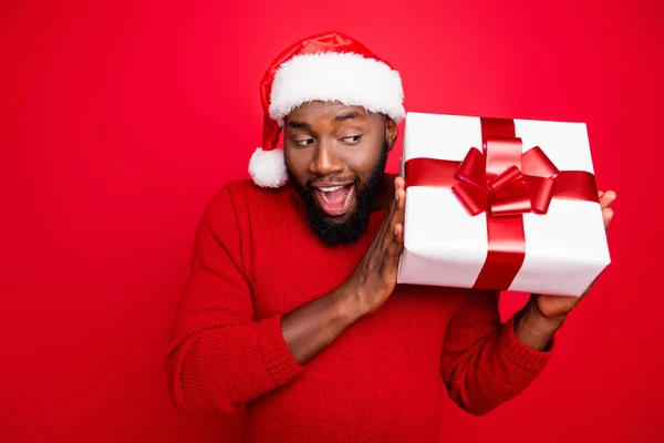 Nahaufnahme Foto von erstaunt Student in Weihnachten Mütze schütteln Paket mit Band für Weihnachten schreien wow tragen Pullover isoliert über rotem Hintergrund — Stockfoto