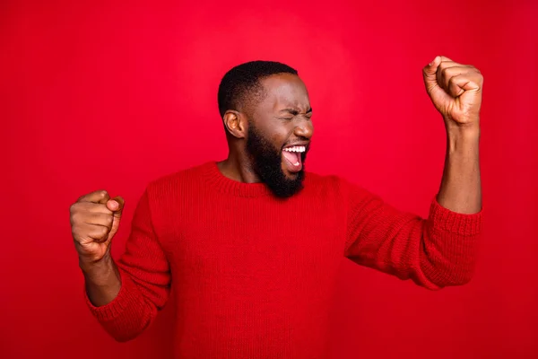 Retrato de homem encantado levantando seus punhos gritando sim comemorar festa do ano novo vestindo camisola na moda isolado sobre fundo vermelho — Fotografia de Stock