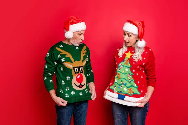 Photo of two astonished excited people grey white haired husband wife showing funny cartoon pictures on reindeer evergreen tree on jumpers isolated bright color background — Stock Photo, Image