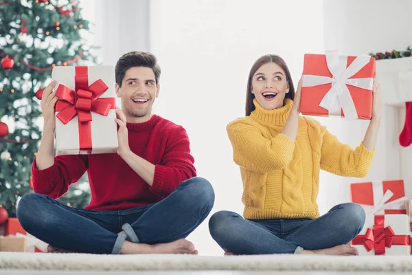 Mmm... menarik. Apa itu. Foto penuh dari dua orang yang terkejut memegang hadiah kocok dari santa yang diterima pada saat Natal menikmati tradisi tahun baru duduk di lantai rumah dengan hiasan x-mas — Stok Foto