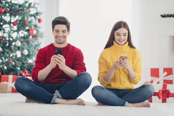 Pełna długość zdjęcia dwóch wesoło romantycznych ludzi siedzieć na podłodze używać telefonu typu Gratulacje z nowyroku Szukaj świąteczne rabaty sezonu w domu z x-mas dekoracji — Zdjęcie stockowe