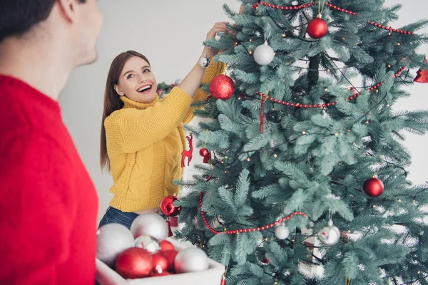 Achterzijde portret van twee mensen vrolijke vrouw versieren Evergreen Fir Tree hand kerstballen genieten van voorbereiding voor x-mas Nieuwjaar viering slijtage rode gele trui in huis — Stockfoto