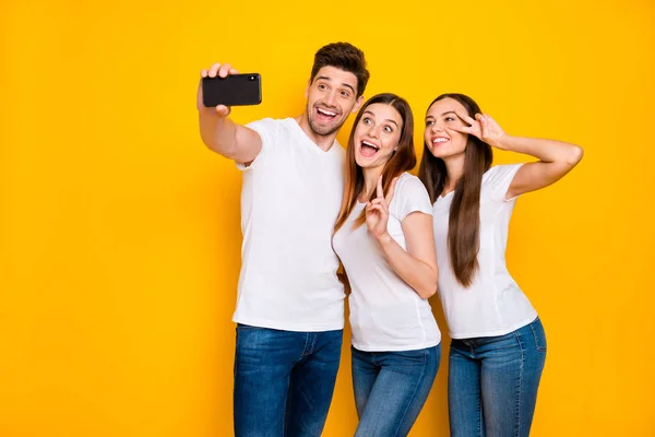 Retrato de três agradável atraente alegre alegre brincalhão brincalhão pessoa positiva infantil tomando fazer selfie se divertindo mostrando v-sinal isolado sobre brilhante brilhante brilho fundo amarelo — Fotografia de Stock