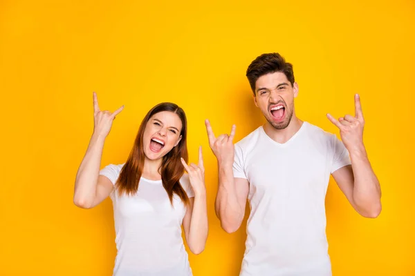 Retrato de duas pessoas legais com corte de cabelo longo fazendo chifres gritando vestindo camiseta branca isolada sobre fundo amarelo — Fotografia de Stock