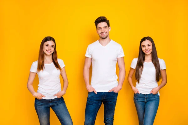 Retrato de pessoas encantadoras com cabelos longos sorrindo colocando as mãos em bolsos usando jeans jeans jeans branco t-shirt isolado sobre fundo amarelo — Fotografia de Stock
