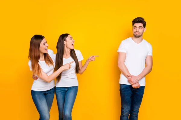 Retrato de una persona confundida mirando a chicas divertidas burlándose de usar una camiseta blanca vaqueros aislados sobre fondo amarillo —  Fotos de Stock