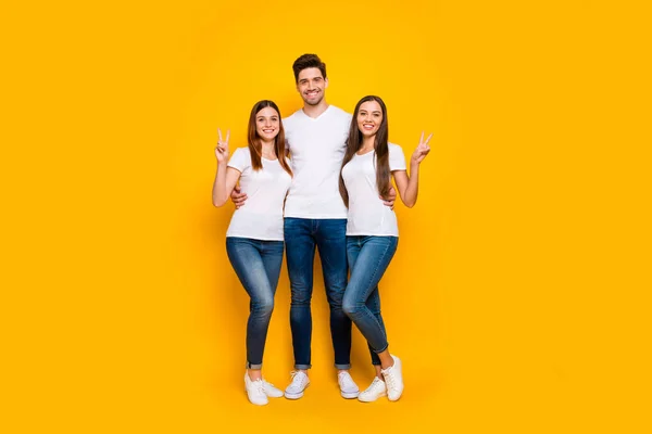 Foto de comprimento total de pessoas positivas em t-shirt branca fazendo v-sinais vestindo jeans jeans isoladas sobre fundo amarelo — Fotografia de Stock