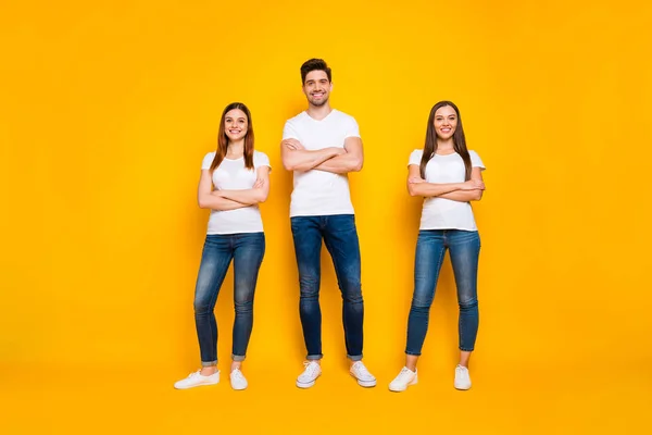 Foto em tamanho completo de amigos positivos com o sorriso dos dentes cruzando as mãos vestindo camiseta branca isolada sobre fundo amarelo — Fotografia de Stock