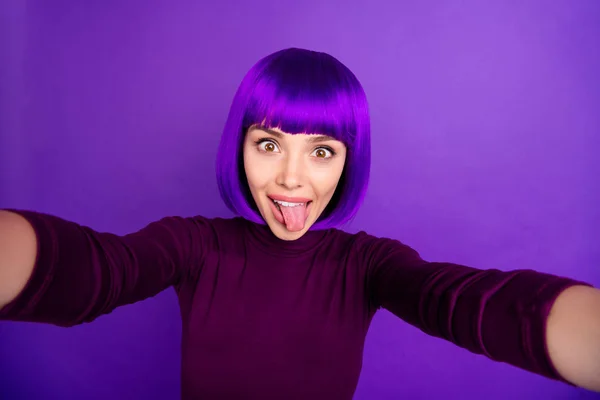 Bonita dama haciendo fotos de uno mismo pegando lengua fuera de la boca desgaste ropa de moda y peluca aislado fondo púrpura —  Fotos de Stock