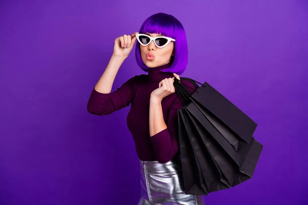 Красива стильна дама тримає багато пакетів в руках відправляє повітряний поцілунок, одягнений в модний одяг ізольований фіолетовий фон — стокове фото