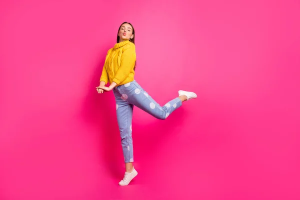 Foto in voller Länge von niedlichen Jugend hebt ihr Bein Senden Luftkuss tragen gelben Pullover gepunktete Jeans isoliert über Fuchsia Hintergrund — Stockfoto