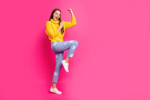 Foto a figura intera di ragazza estatica alzando i pugni urlando sì indossando maglione giallo punteggiato jeans denim isolato su sfondo fucsia — Foto Stock