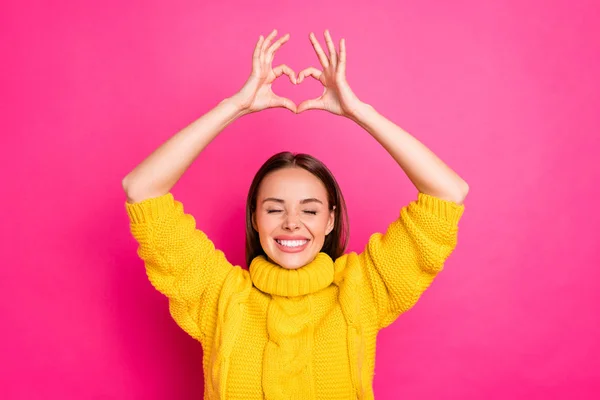 Close up foto de menina alegre mostrando coração figura coração apreciando vestindo suéter amarelo isolado sobre fundo fúcsia — Fotografia de Stock