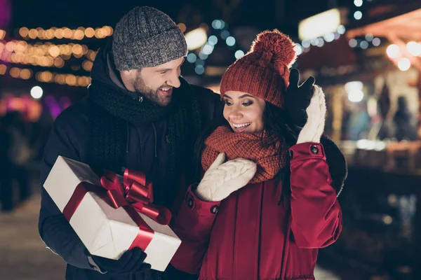 Foto de cara amoroso entregando linda senhora tradicional x-mas giftbox com arco vermelho romance momento vestindo casacos quentes de malha bonés e lenços ao ar livre — Fotografia de Stock