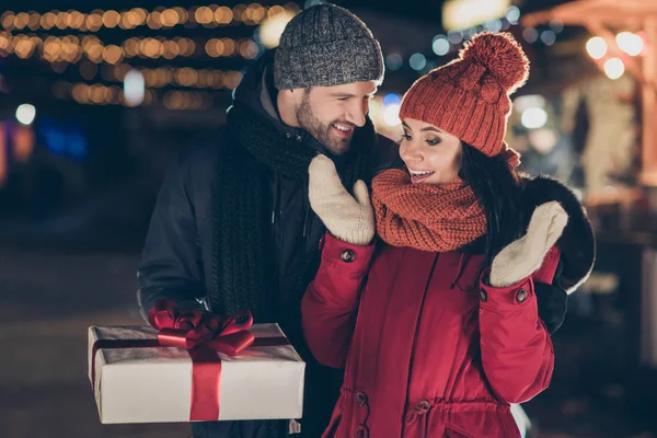 暖かいコートを着て赤い弓新年の伝統を持つかわいい女性X-masギフトボックスを提供する男の写真は、屋外でキャップとスカーフを編みました — ストック写真