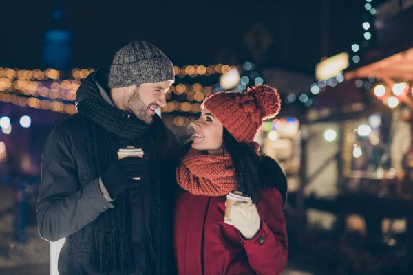 Foto de duas pessoas bonitas emparelhar com bebida quente em mãos celebrando x-mas noite feliz juntos vestindo casacos quentes de malha chapéus e lenços ao ar livre — Fotografia de Stock