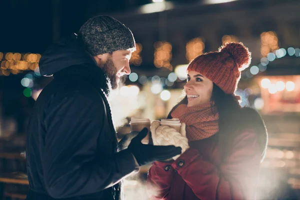 Фото двох чарівних людей з гарячим чаєм в руках, що святкують Різдвяну ніч в чарівній атмосфері на відкритому повітрі в теплих куртках — стокове фото