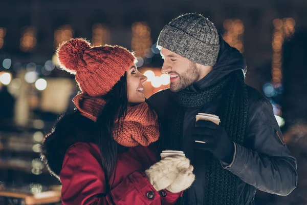 Фотографія двох ласкавих людей з гарячим чаєм в руках, що святкують Різдво в чарівній атмосфері в теплих пальто зовні — стокове фото