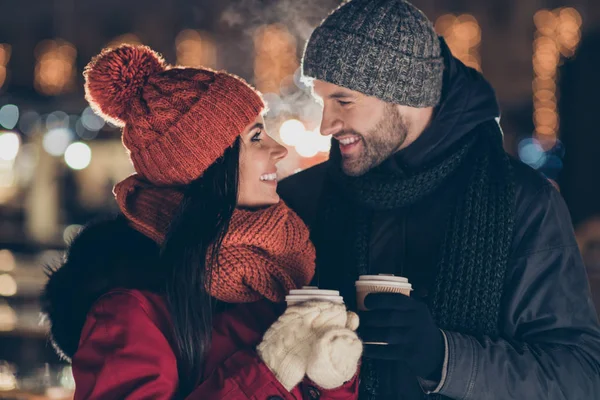 Photo of two cute people with hot tea beverage in hands celebrating x-mas eve in magic street atmosphere wearing warm coats outside