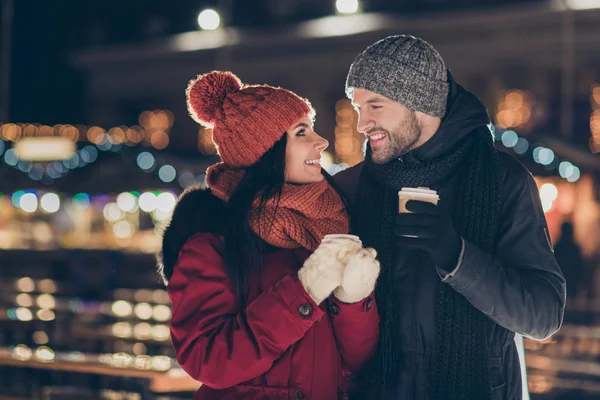 Фото двох людей з гарячим чаєм в руках, що святкують Різдвяну ніч в чарівній атмосфері на відкритому повітрі в теплих куртках — стокове фото
