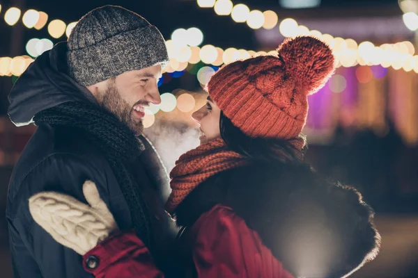 Foto von zwei verliebten verliebten Liebespaaren an Weihnachten Mitternacht beleuchteten Straßen stehen einander gegenüber und küssen sich in warmen Jacken draußen — Stockfoto