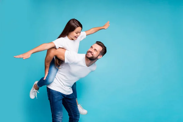 Profile side photo of cheerful people holding hands playing piggyback wearing white t-shirt denim jeans isolated over blue background — Stock Photo, Image