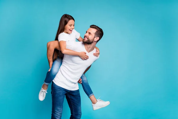 Retrato de un hombre alegre sosteniendo a su hijo con un peinado moreno a cuestas con camiseta blanca vaqueros de mezclilla aislados sobre fondo azul — Foto de Stock