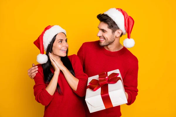 Retrato de homem bonito em chapéu xmas dar pacote para sua esposa impressionada usar pulôver vermelho isolado sobre fundo amarelo — Fotografia de Stock