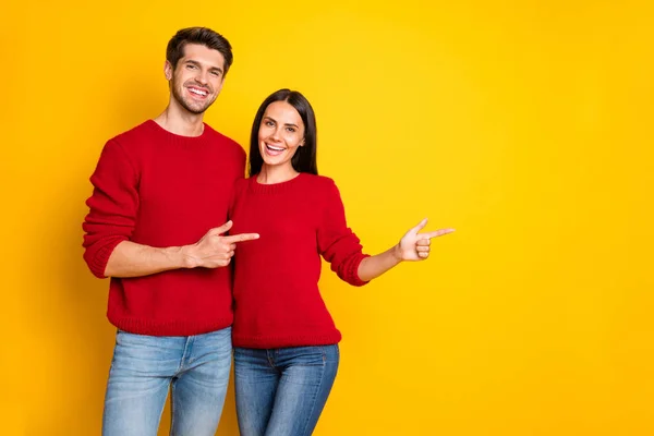 Portrait of charming spouses point at copy space recommend ads wear red pullover sweater denim jeans isolated over yellow background — Stock Photo, Image