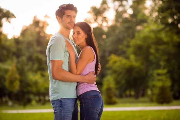 Portrait of dreamy spouses hugging closing eyes wearing t-shirt denim jeans outside — Stok fotoğraf