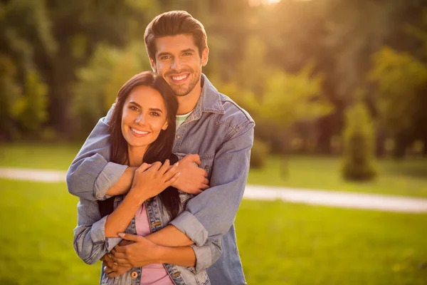 Portrait of lovely spouses with brunet hairstyle cuddling piggyback standing on green lawn wearing denim jeans jacket blazers outside — Stock Photo, Image