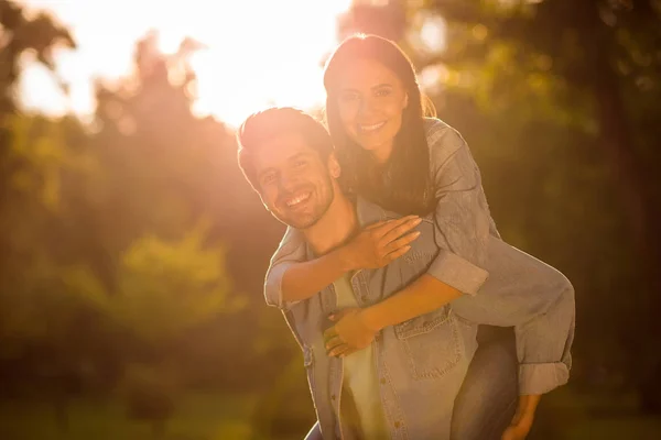 Närbild foto av charmig flicka och kille piggyback stående i skogen under solen bär denim jeans jackor utanför — Stockfoto