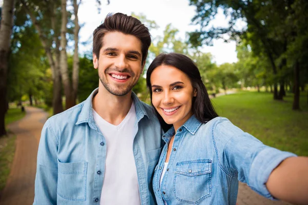 Закройте фотографию веселой супружеской пары, делающей фото улыбающейся в джинсовой рубашке на улице в лесу — стоковое фото