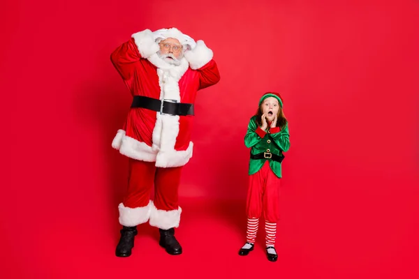 Celá tělíčka užaslého Santa Clause s vnučkou v kostýmech zeleného skřítka, viz Noel neuvěřitelný zázrak nosí brýle s brýlemi izolovanými přes červené pozadí — Stock fotografie