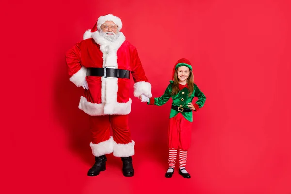 Photo pleine longueur de charmant elfe Père Noël en chapeau coiffure tenant les mains prêtes à profiter de la nuit de Noël en portant une ceinture de costume vert brillant isolé sur fond rouge — Photo